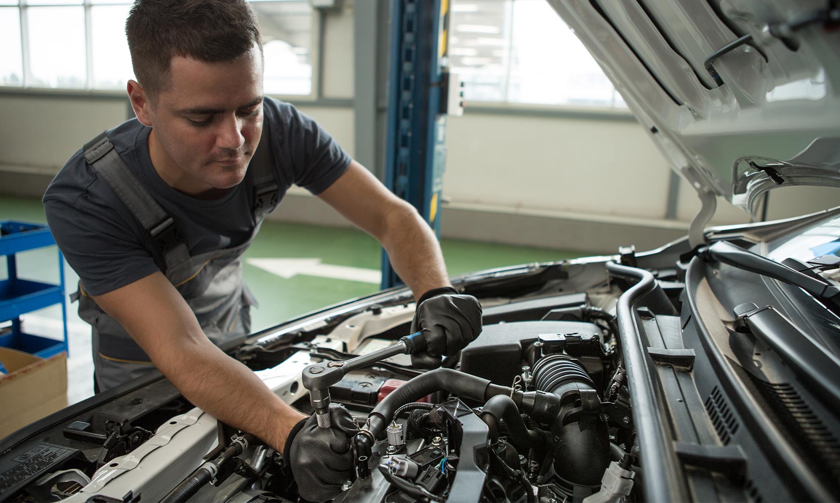 A mechanic under the hood of car, working on the engine with a ratchet.