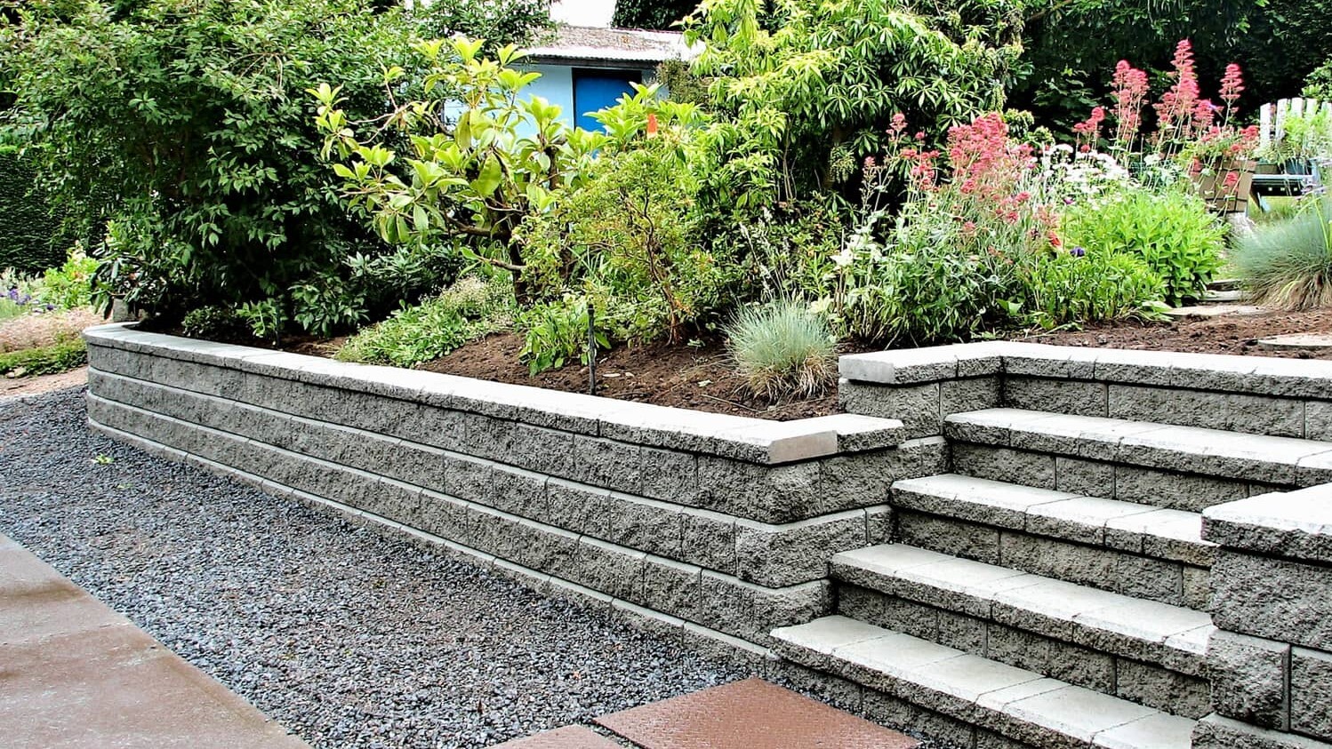 A beautiful stone retaining wall with lush greenery and flowers, creating a peaceful and natural landscape.