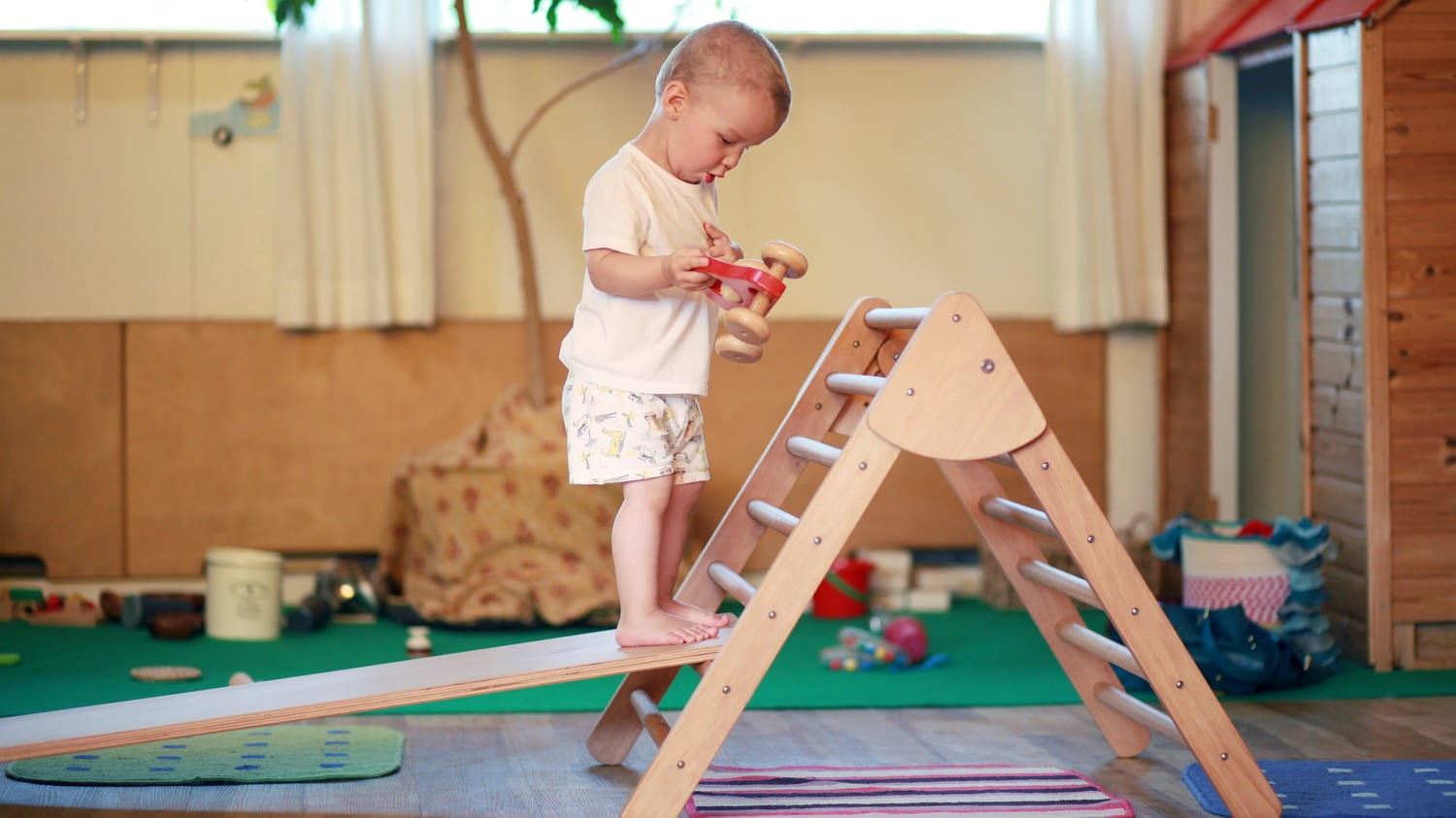 A wooden Pikler triangle, a climbing structure for children, with colorful rungs and a child happily climbing on it.