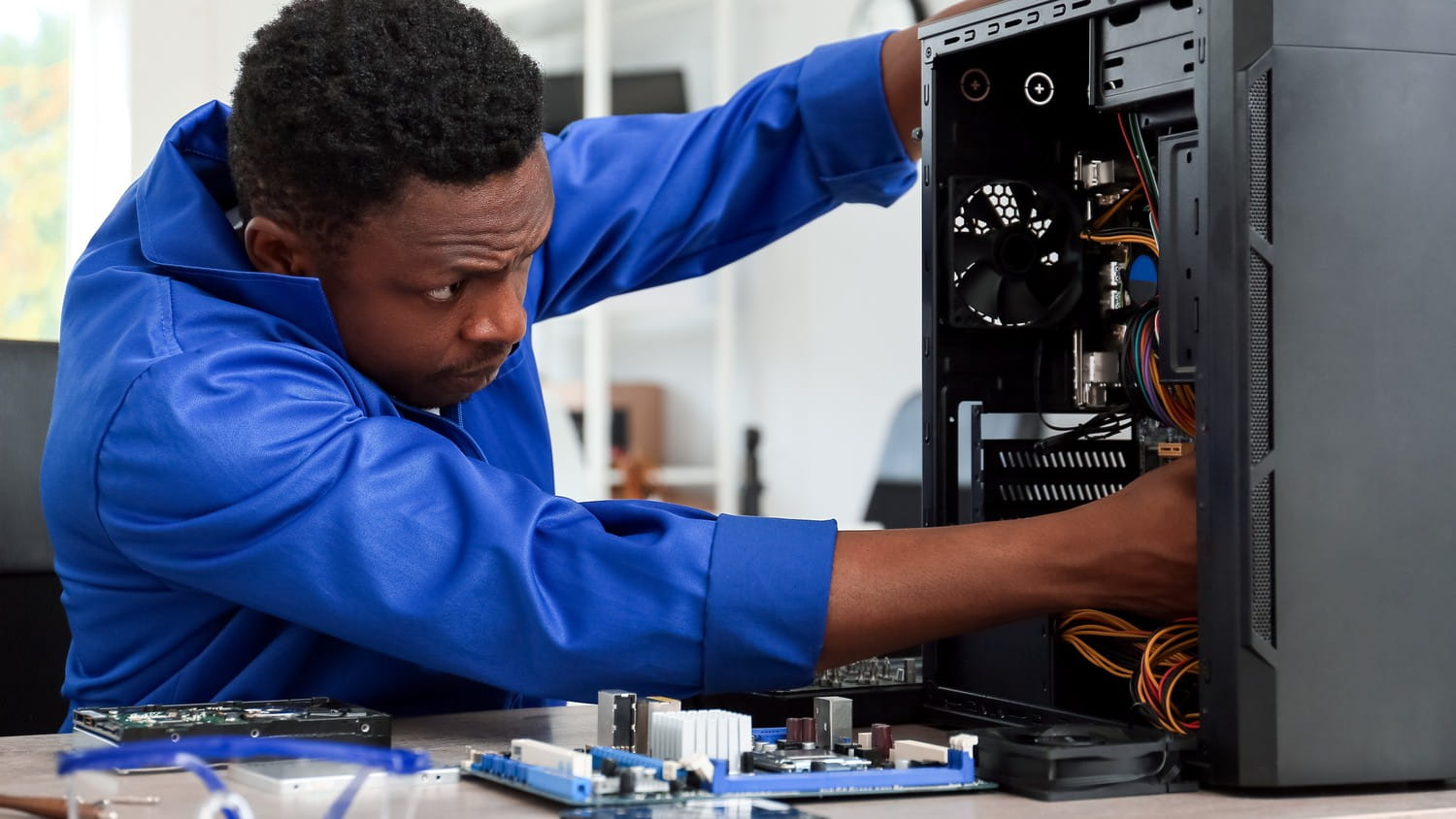 A person assembling a computer, carefully connecting wires and components on a desk with tools and a manual nearby.