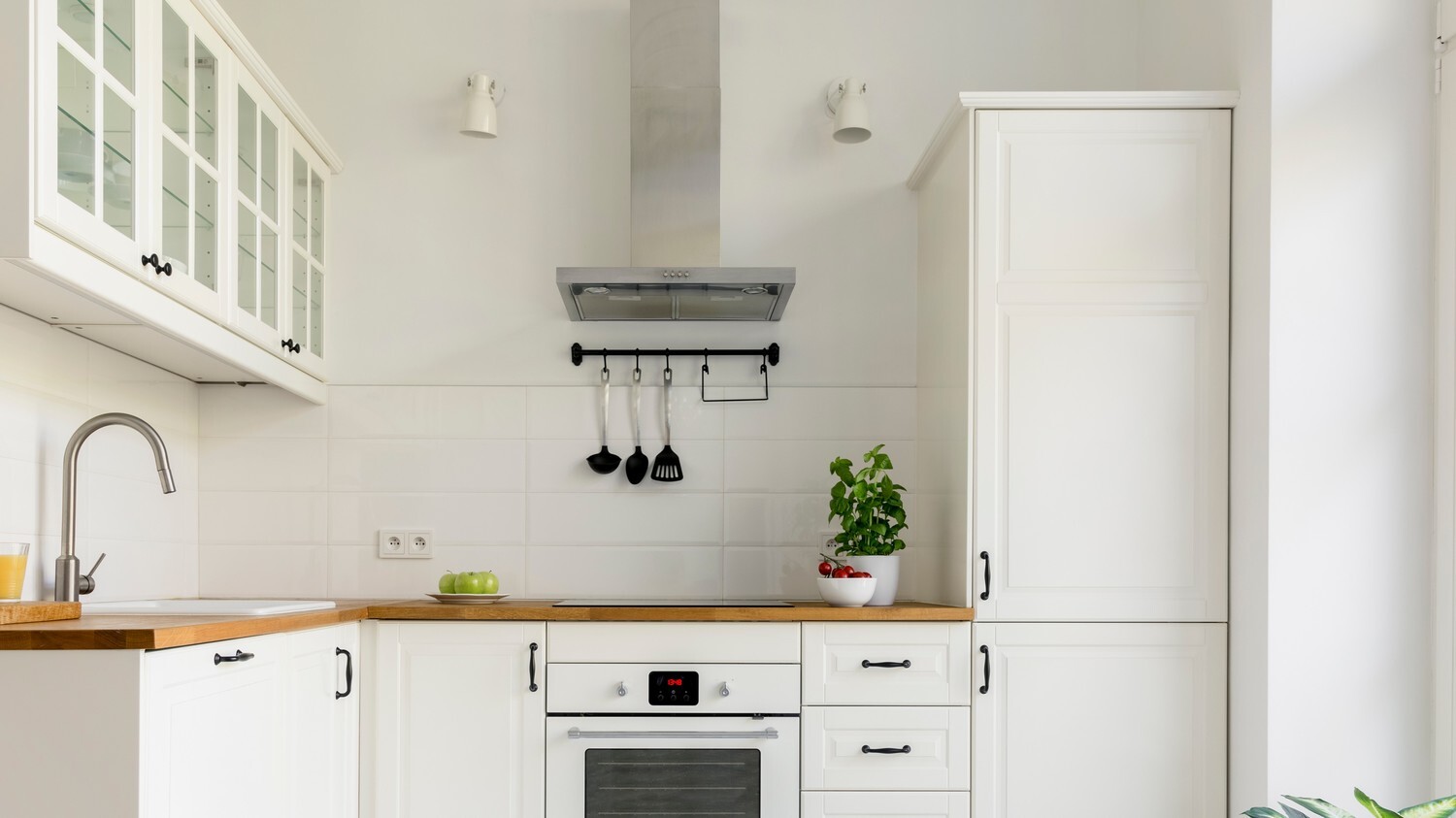 A white, modern kitchen with a rangehood and an oven.
