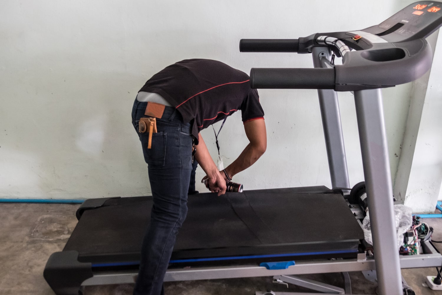 A person repairing a treadmill, focused on fixing the belt and adjusting the tension, with tools and parts scattered around.