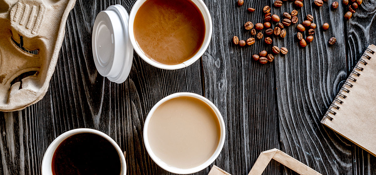 A close-up of a coffee cup, sitting on a wooden table with a blurred background.