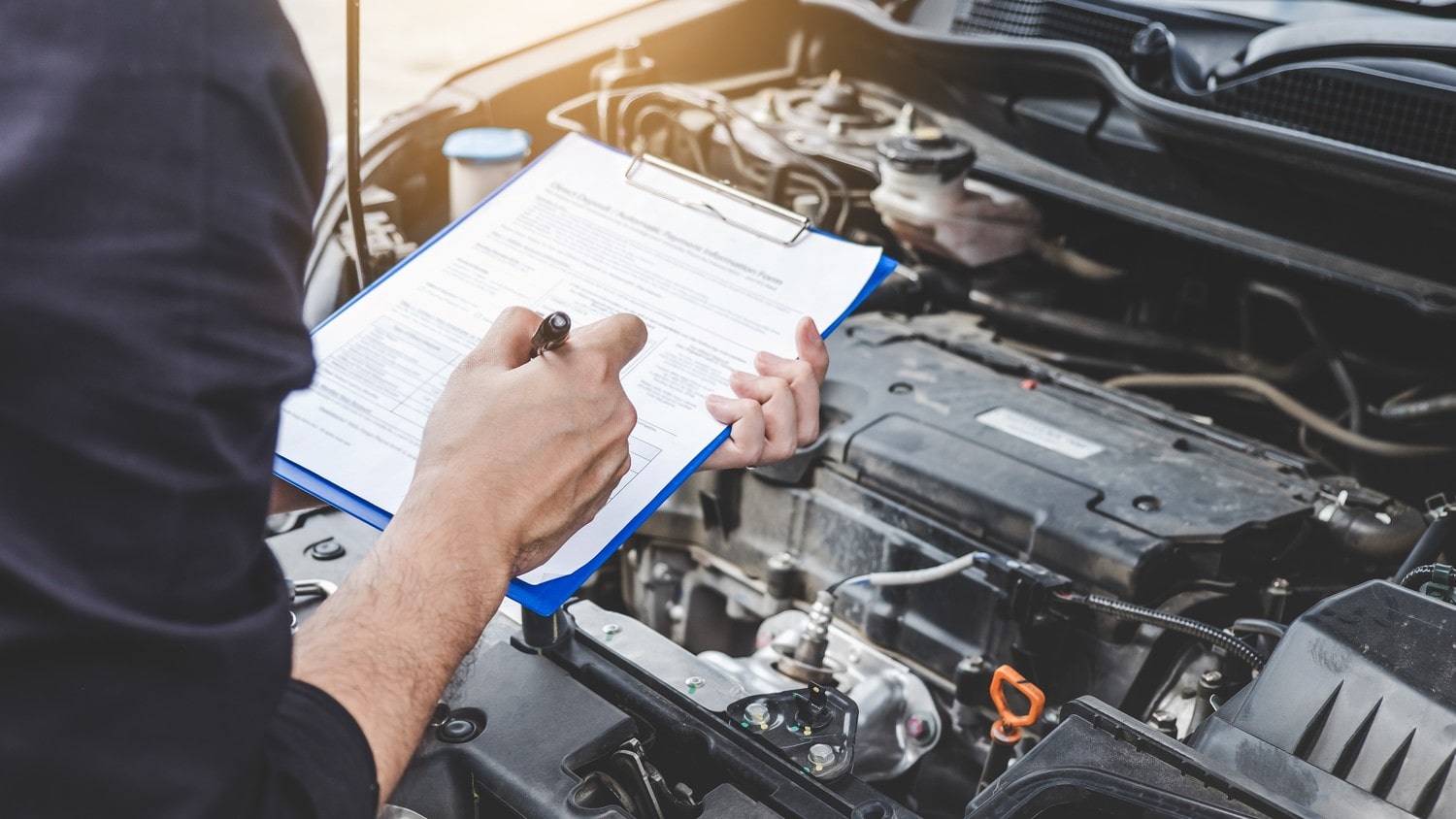 A car inspector making notes while inspecting the engine.