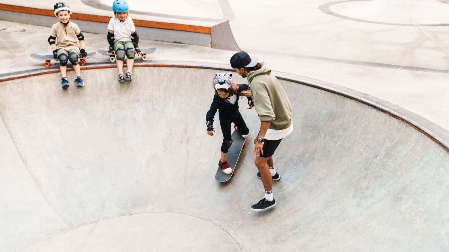 A kid riding a skateboard on a sunny day with a help of an adult.