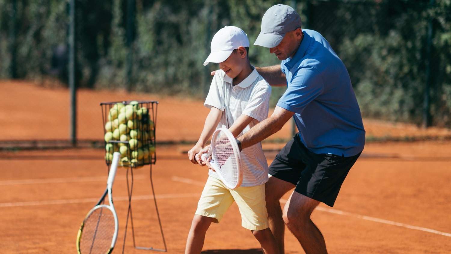 Kid being taught by a tennis instructor on how to swing the racquet.