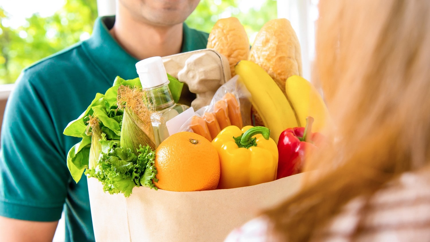 A person delivering groceries that include different fruits.