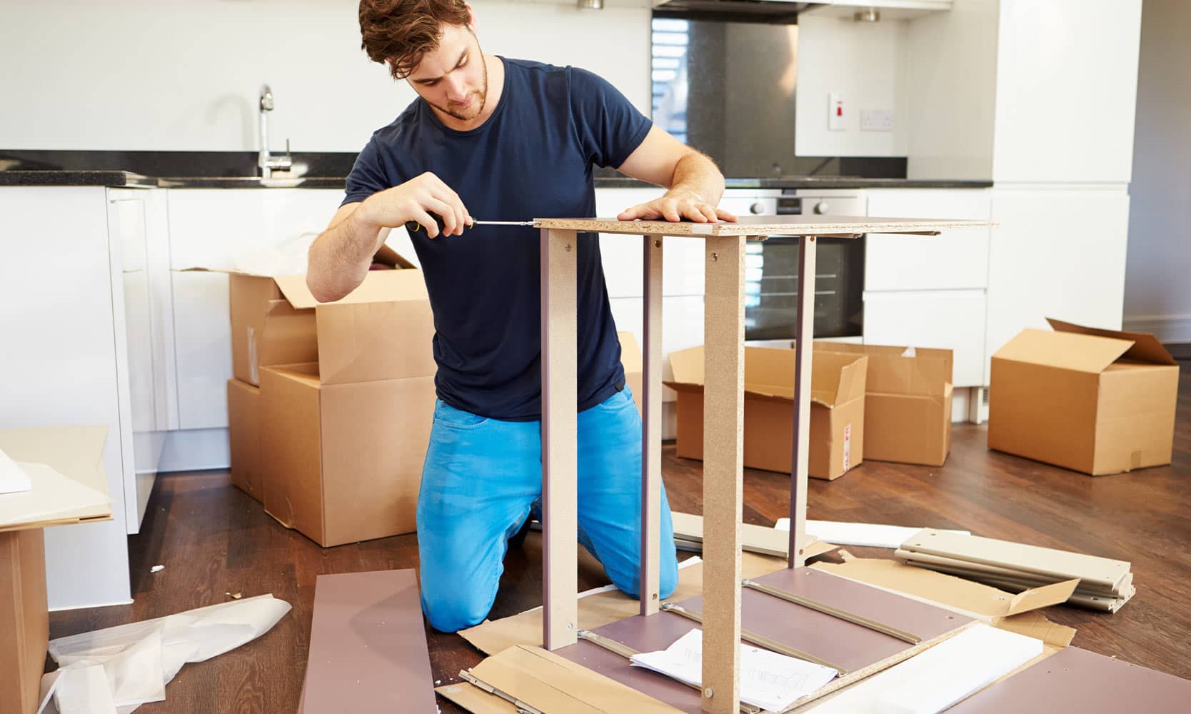 A person assembling furniture with a screwdriver and wrench, surrounded by various furniture parts and tools.