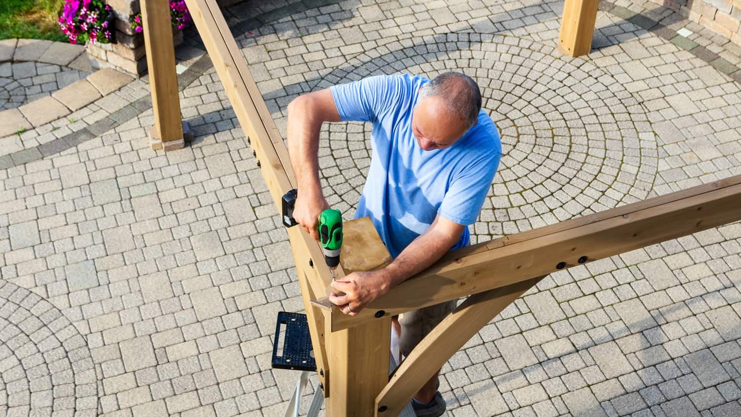 A person working on building a pergolla, drilling the beams together.