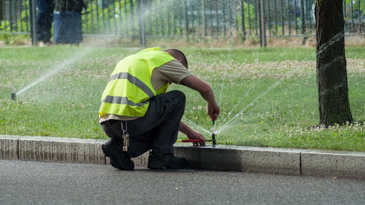 A close-up photo of a person repairing an irrigation system, holding a wrench and adjusting a valve.