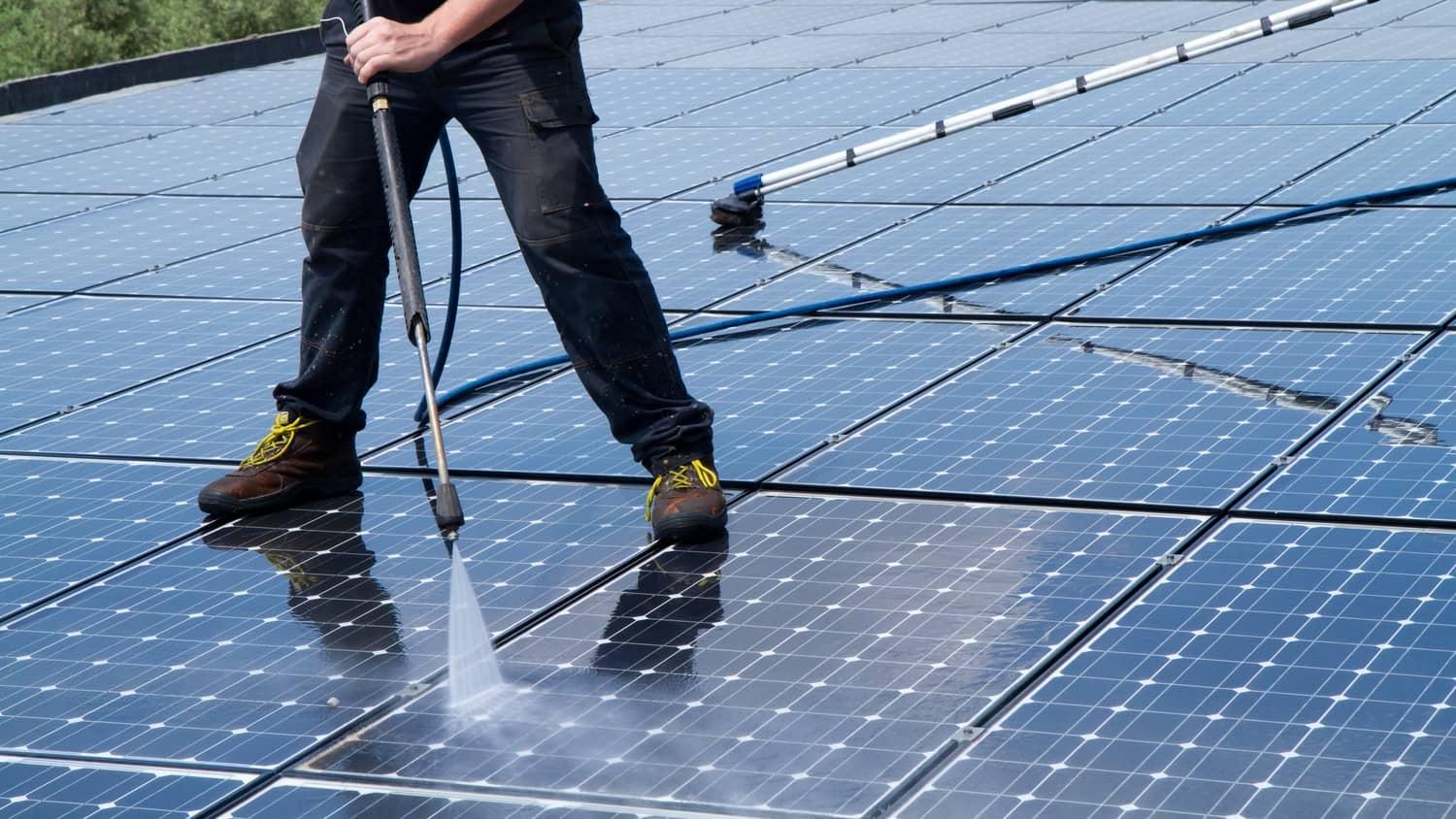 A person cleaning solar panels on a rooftop with a brush and water, ensuring maximum efficiency and energy production.