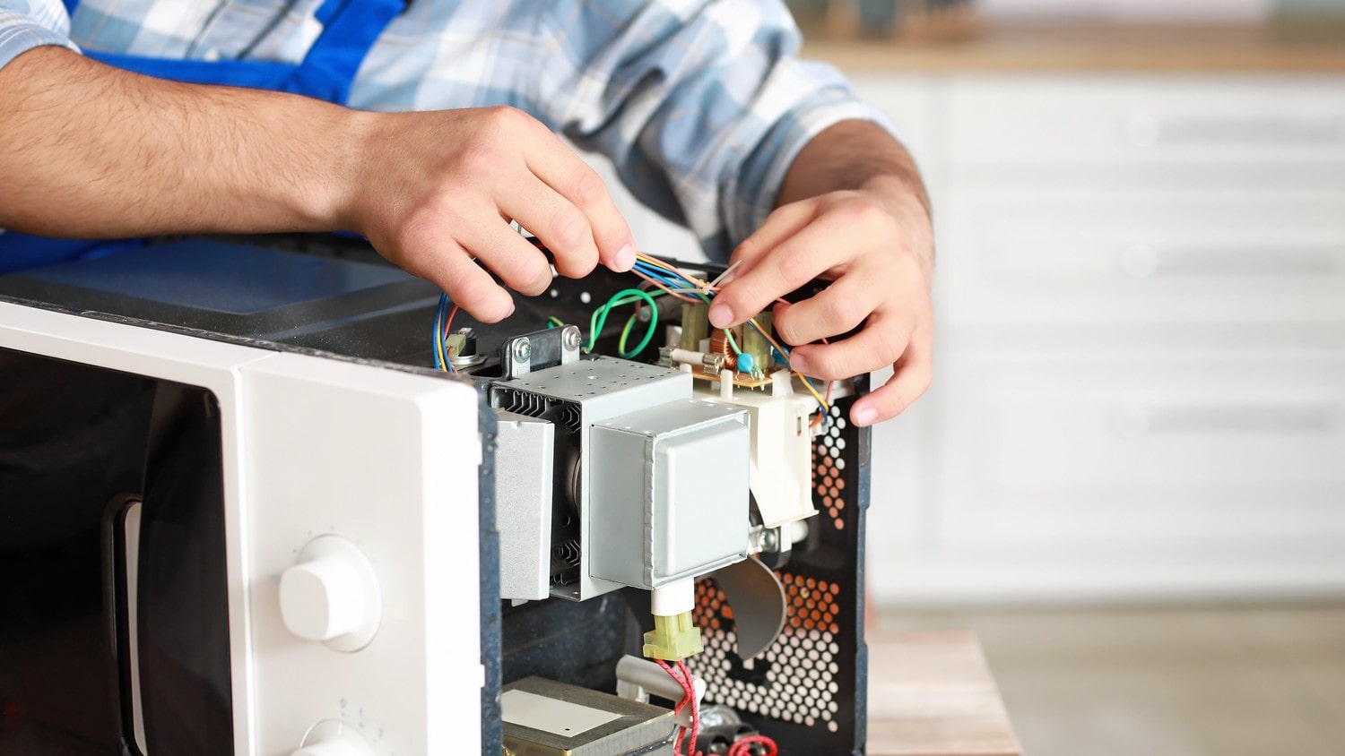 A close-up of a technician repairing a microwave, with tools and wires scattered around.
