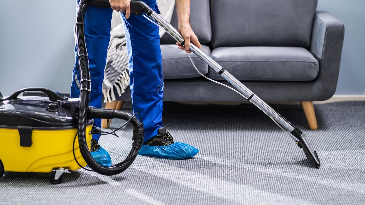 A person using a vacuum cleaner to clean a carpeted floor.