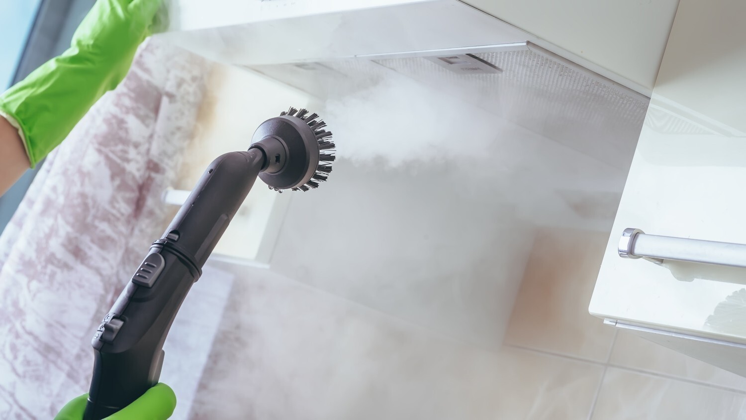A person using a steam cleaner to clean a kitchen range hood.