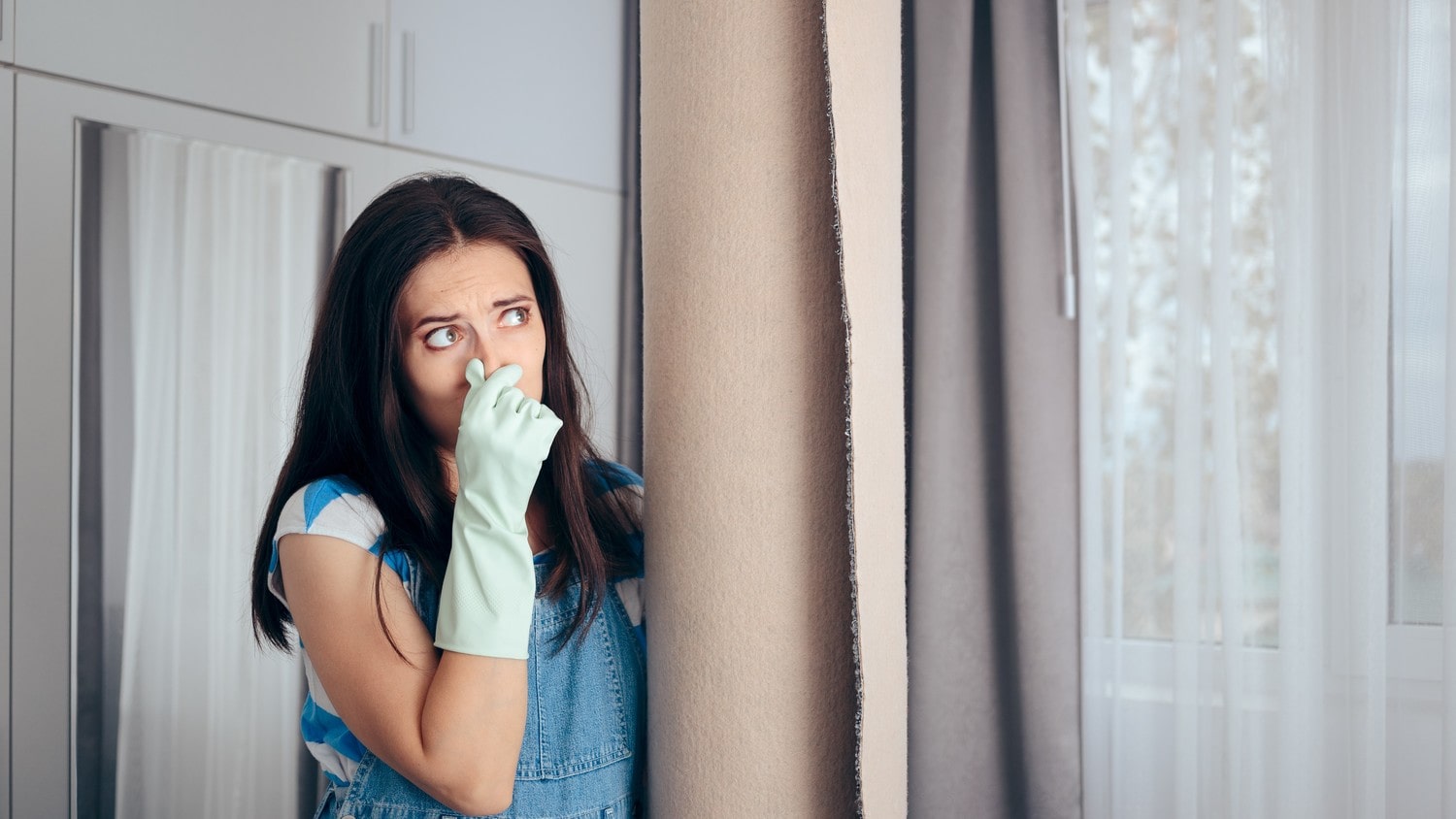 A person wearing gloves, pinching her nose to avoid smelling foul odours from a carpet.