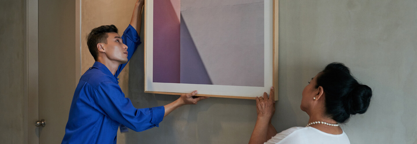 A man and a woman hanging a framed picture, making sure that its level.