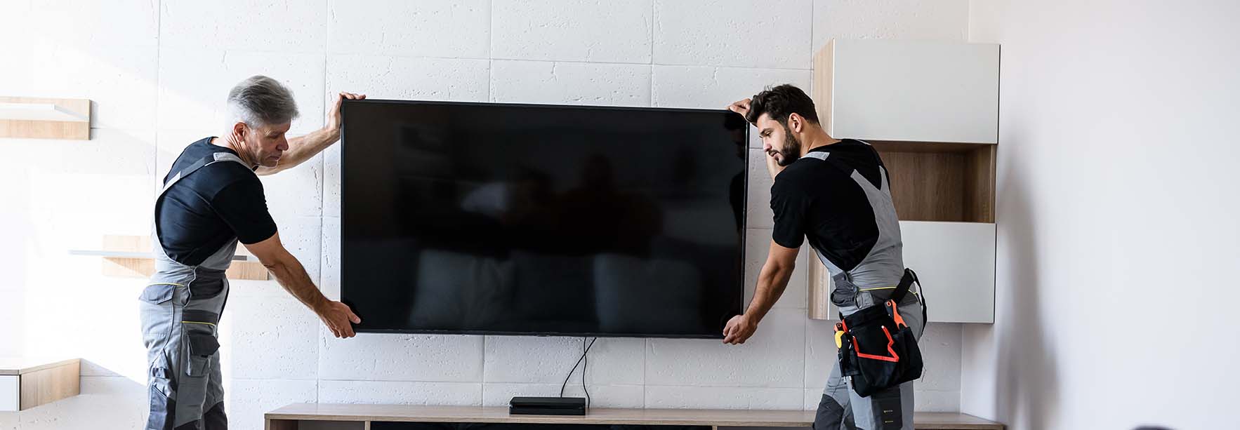 A TV mounted on a wall with cables neatly hidden, installed by two workers.