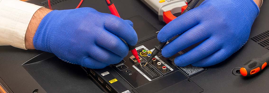 A close-up of a person repairing a television with a screwdriver and a circuit board, surrounded by various tools and electronic components.
