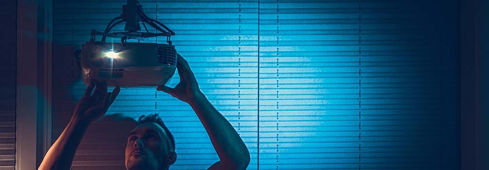 A person installing a projector on the ceiling of a dark room.