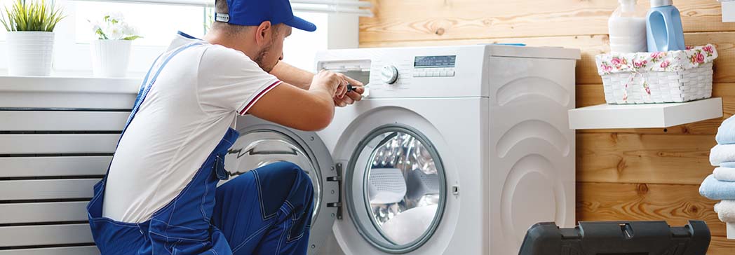 A close-up of a person repairing a washing machine, with tools and parts scattered around.