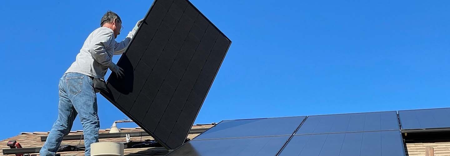 A team of workers installing solar panels on a rooftop, with blue sky and clouds in the background.