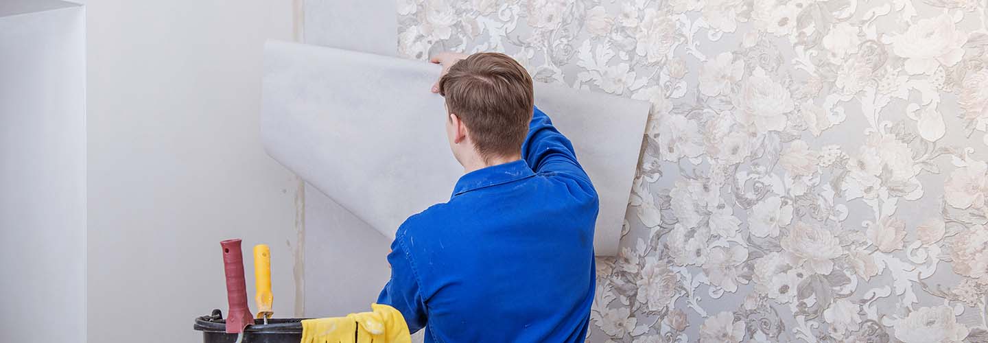 A person carefully installing wallpaper on a wall, using a smoothing tool to remove air bubbles and create a seamless finish.