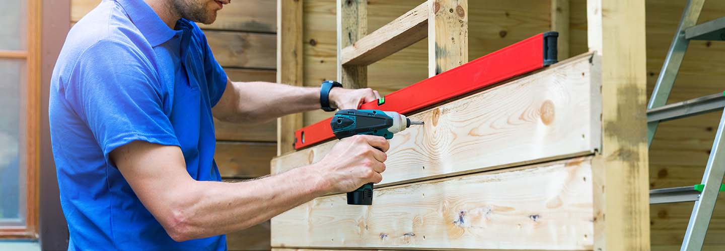 A person assembling a shed in a backyard, surrounded by tools and materials, with a sunny sky in the background.