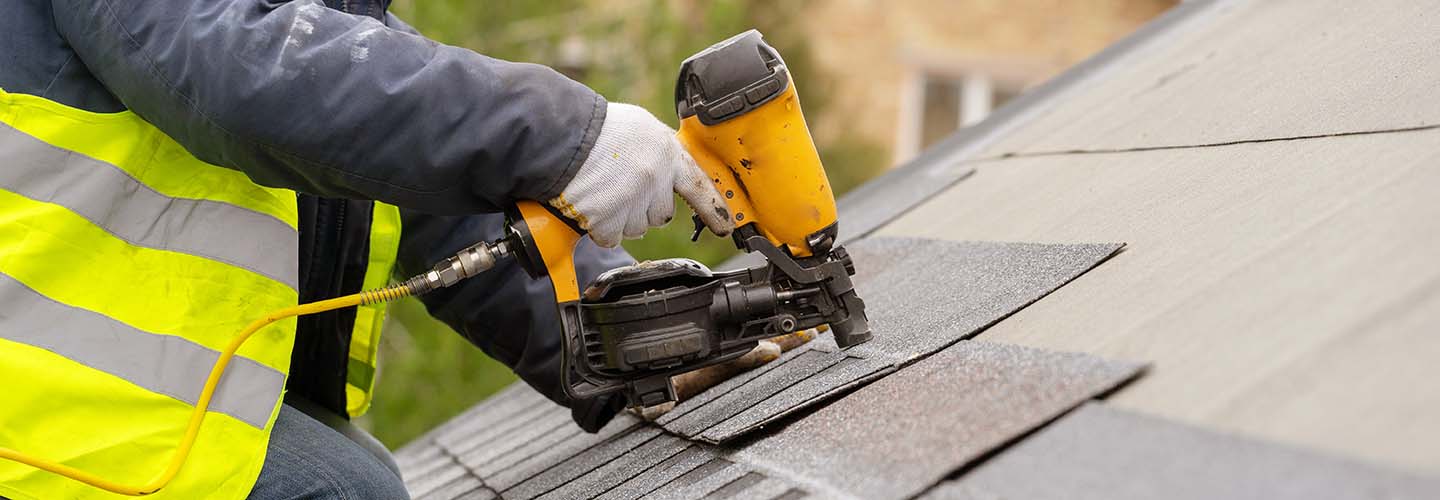 A close-up view of a roofing project, showing workers installing shingles on a house under a clear blue sky.