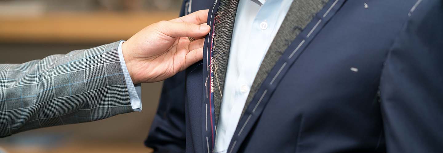 A close-up of a tailor's hands carefully inspecting fabric of a suit.