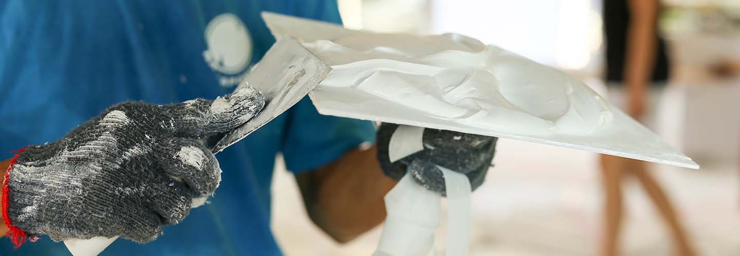 A close up of a person smoothening out plaster on a trowell. 