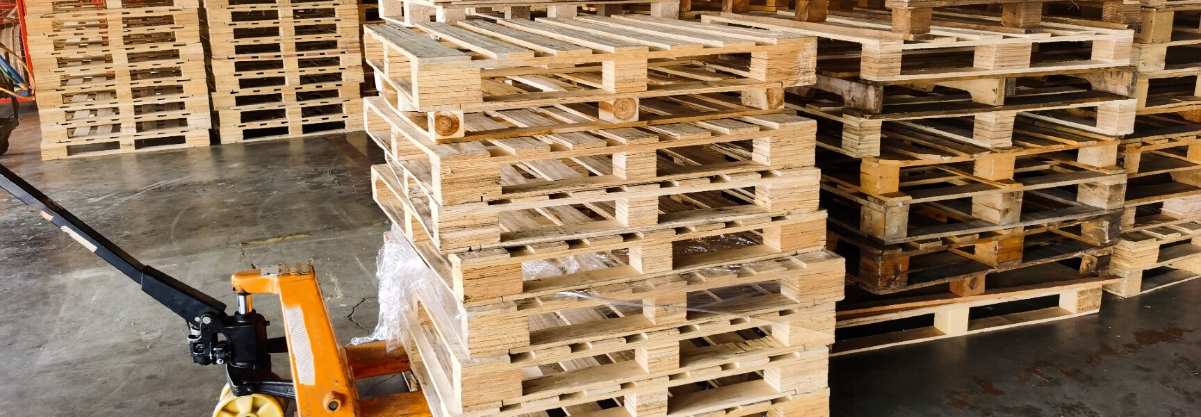 A person collecting pallets from a warehouse, with stacks of wooden pallets in the background.
