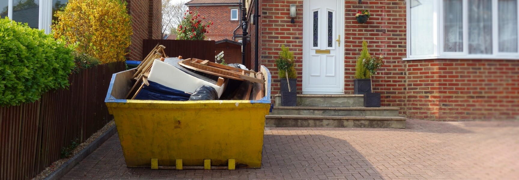 A large green skip bin filled with various types of waste, including cardboard boxes, wood, and construction debris.