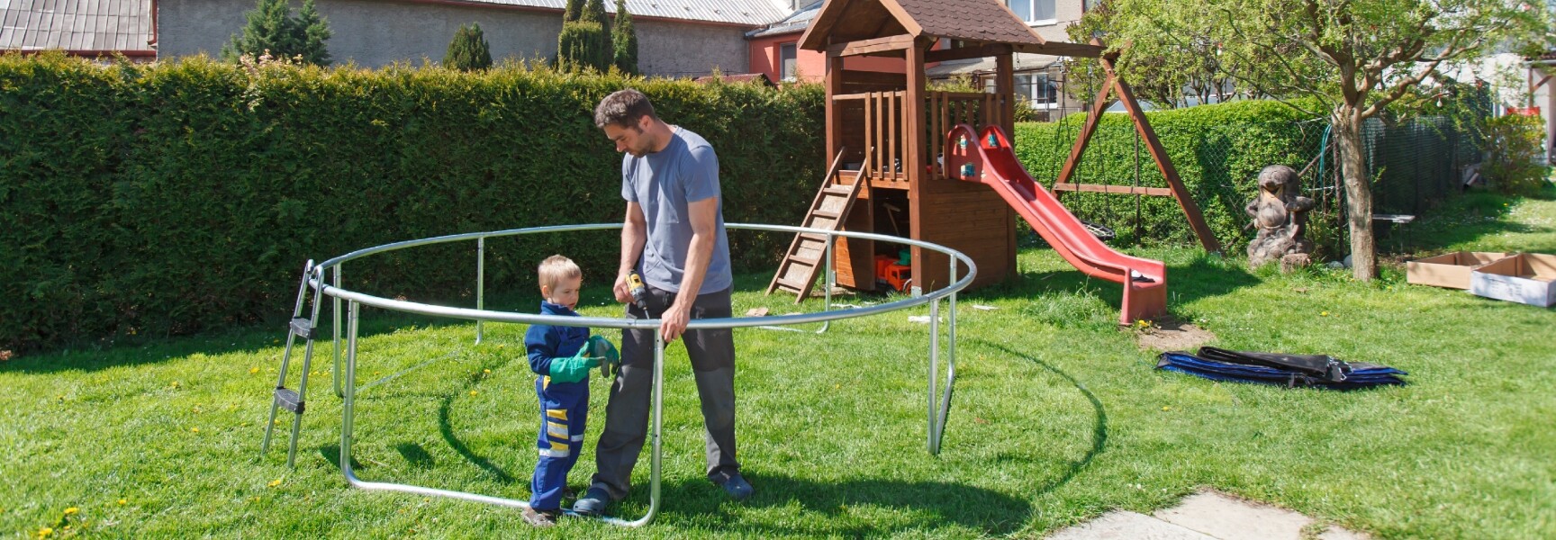 A person assembling a trampoline, with metal frames and springs laid out on the ground, ready to be put together.