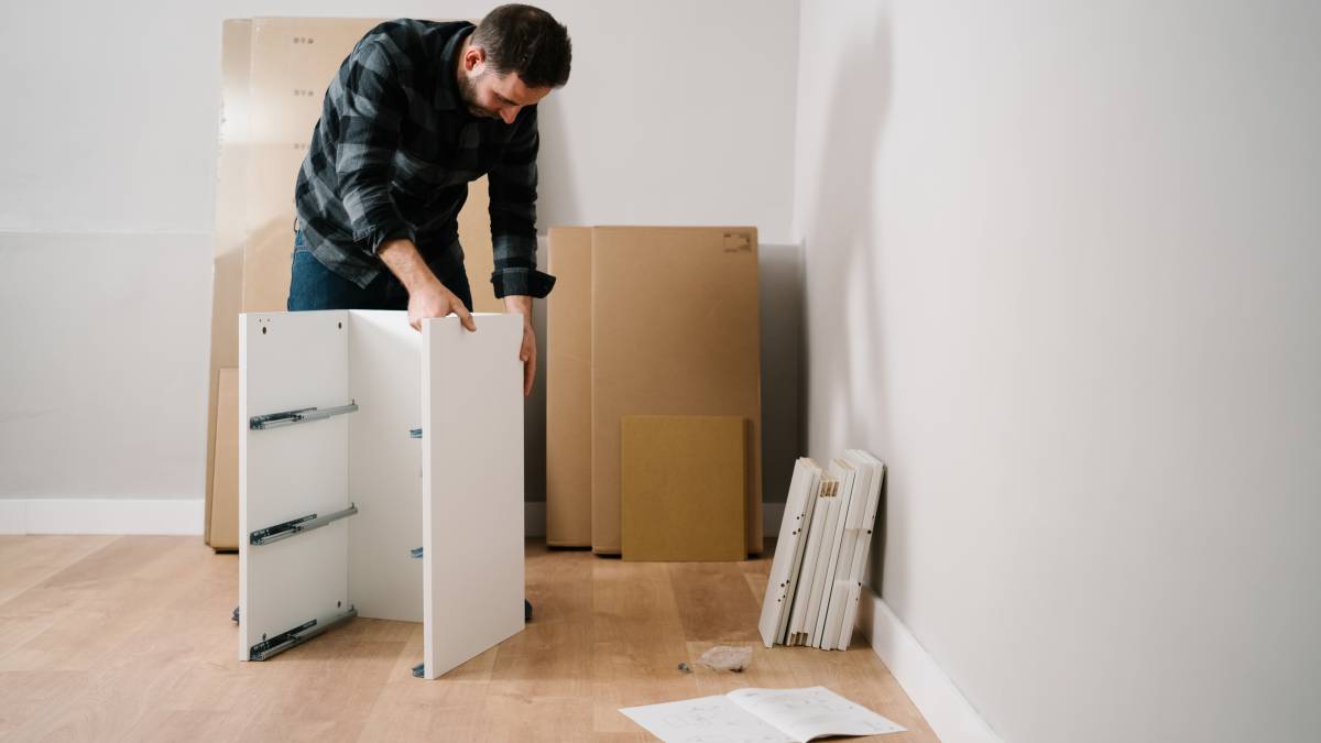 A man engaged in IKEA furniture assembly, aligning cabinet panels on a wooden floor.