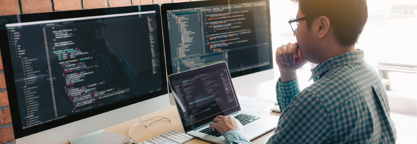 A photo of a web developer working in front of two monitors and his laptop.