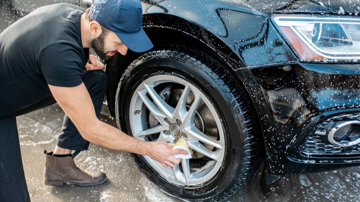 car washing attendant cleaning a car rim with detergent