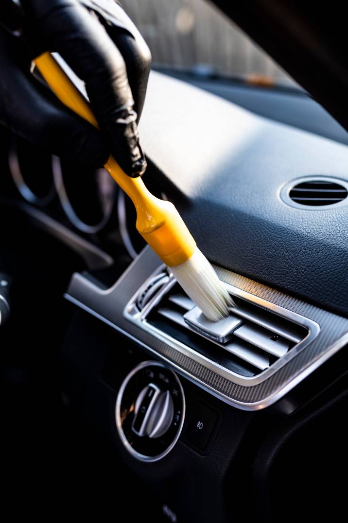a hand holding a brush to clean a car's air-conditioning vents