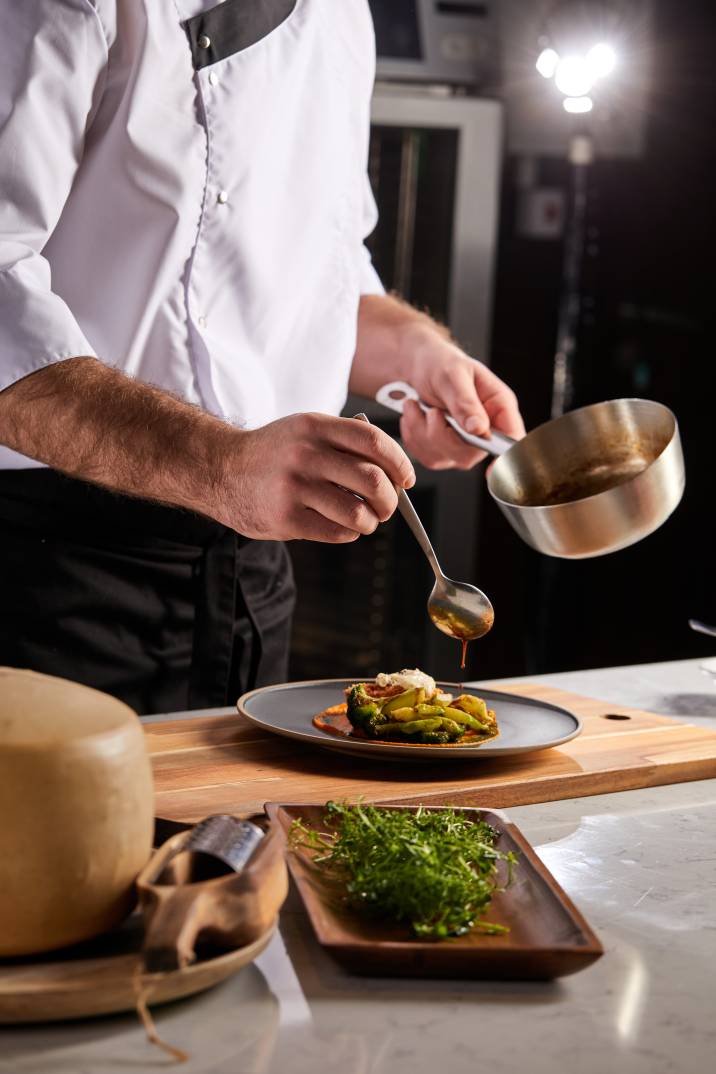 a chef pouring sauce on a vegetable dish