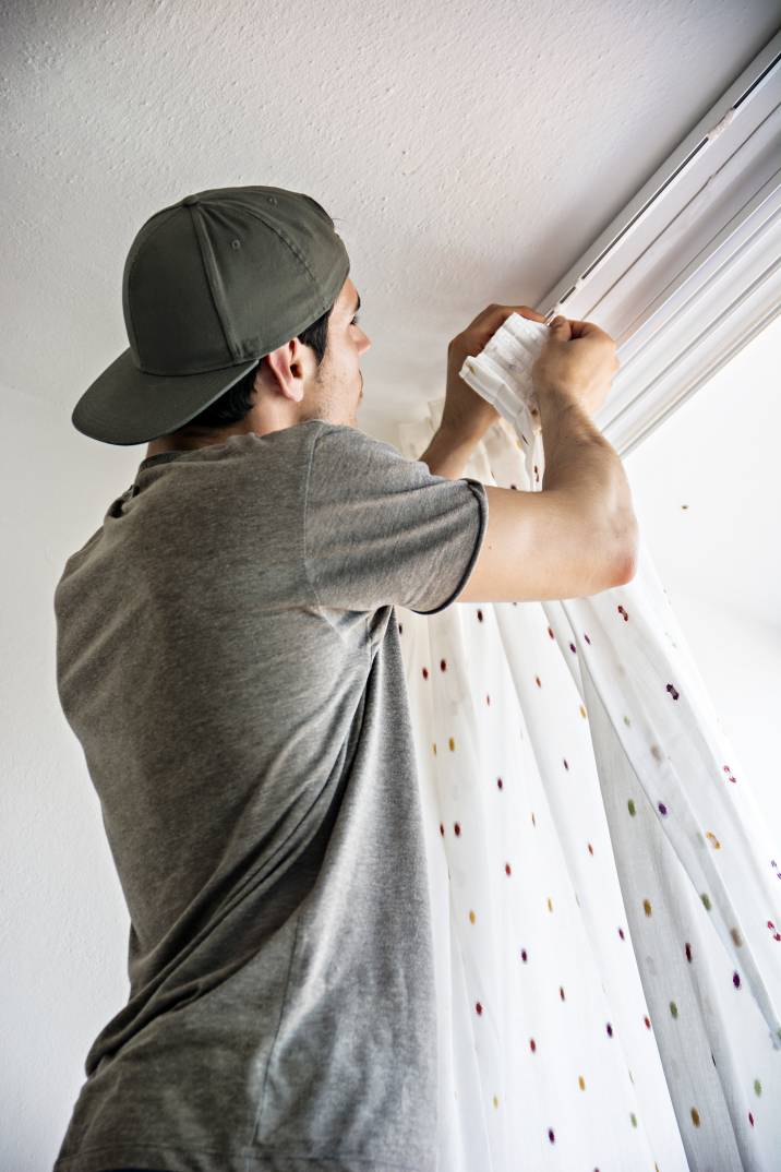 a handyman attaching a curtain to its rod