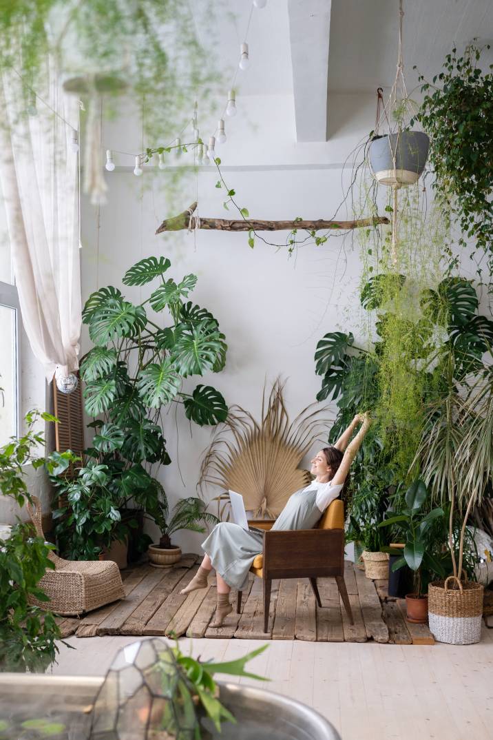 relaxed woman stretching her arms while sitting inside a garden room full of plants