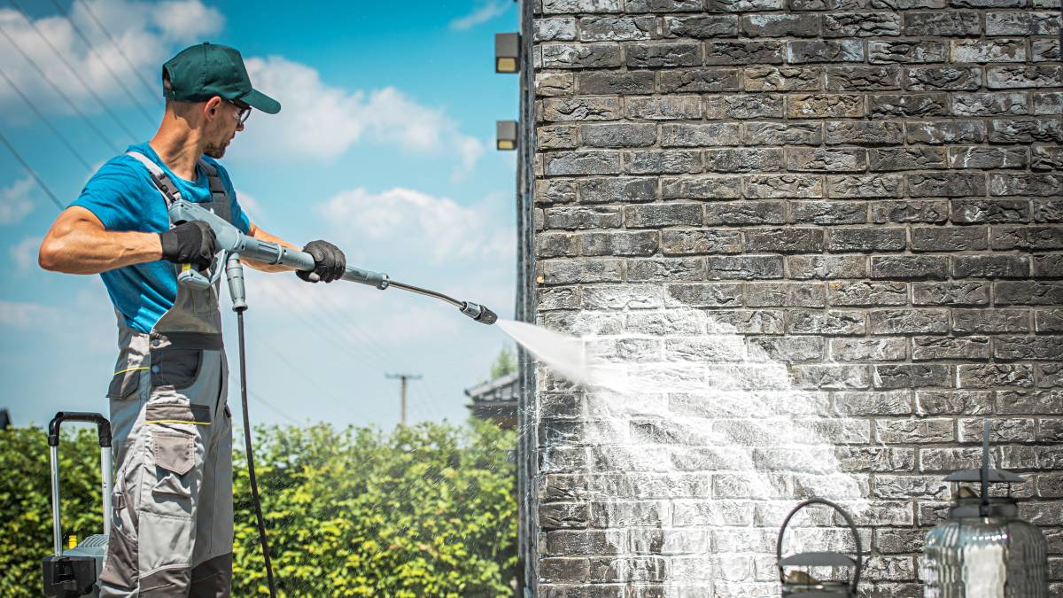 handyman using pressure washer on brick wall