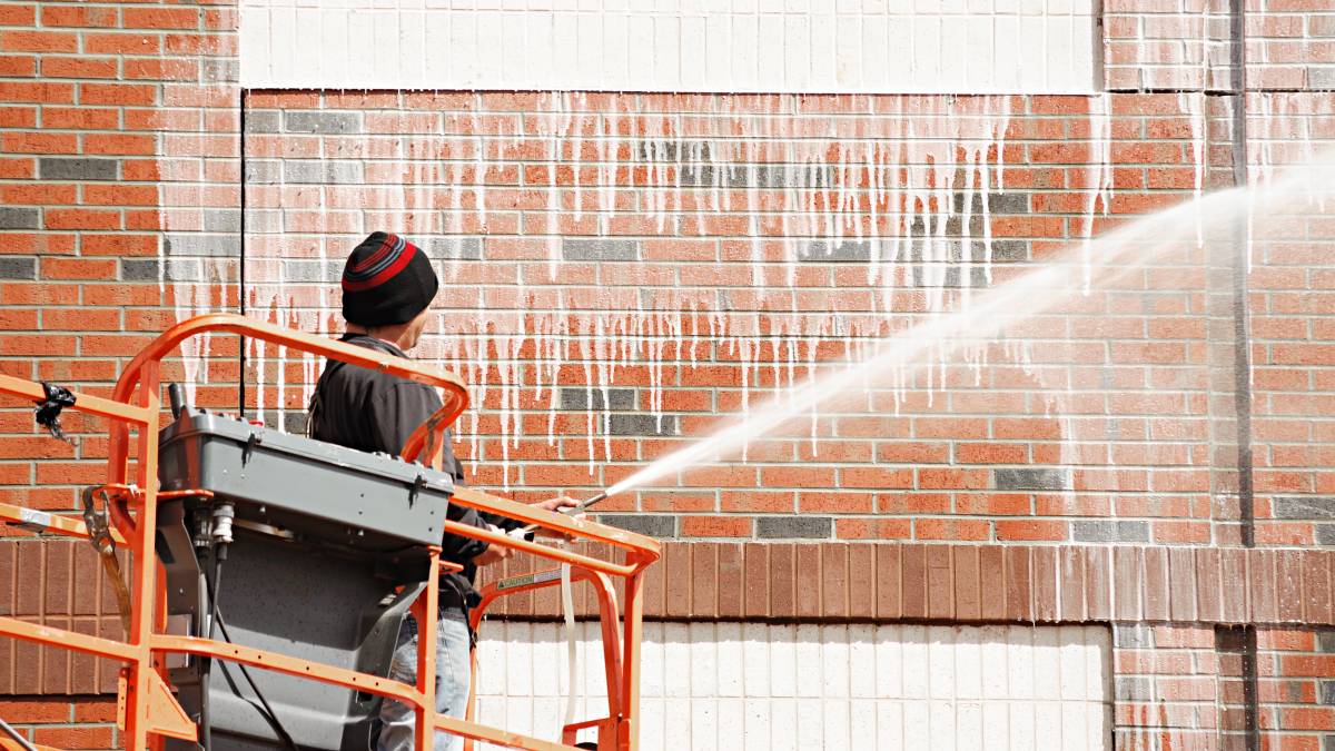 man cleaning brick wall using pressure washer