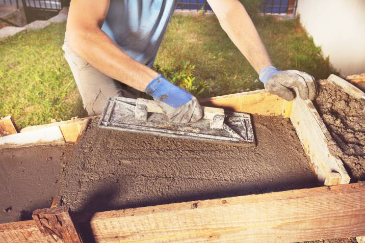 man's hands using a trowel to lay concrete foundation for garden steps