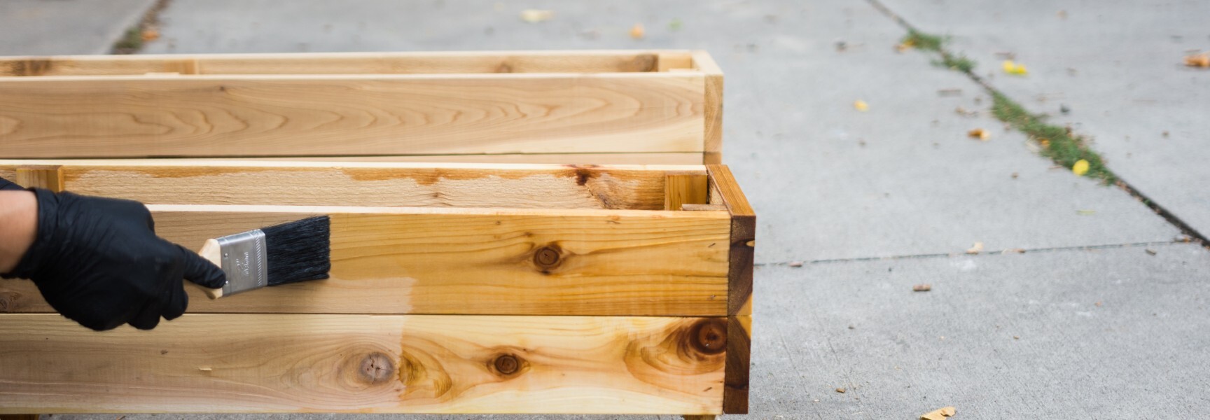 A close-up of a planter box being varnished with a brush.