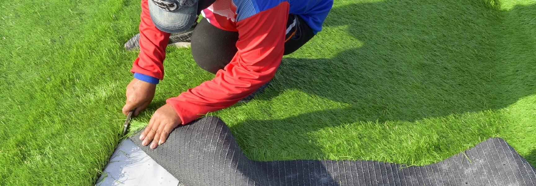 A close-up photo of a person's hand holding a small patch of green turf, with dirt and grass visible in the background.