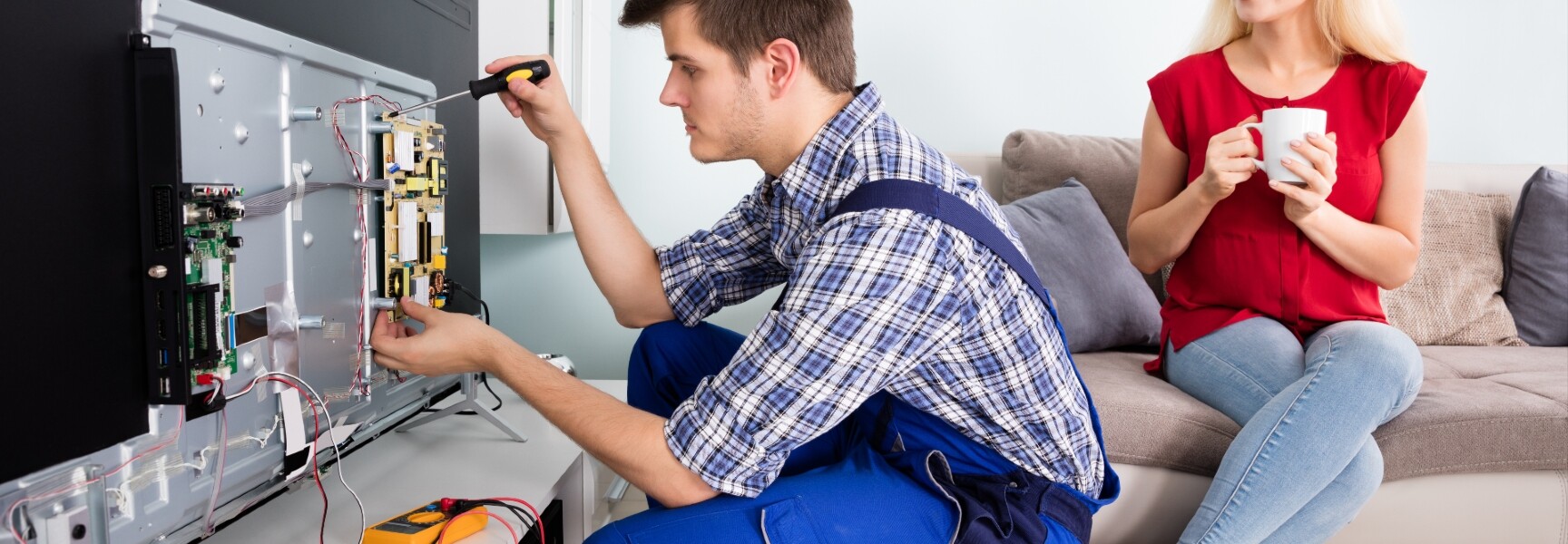 A person setting up a sleek and modern plasma tv in the living room while the owner observes.