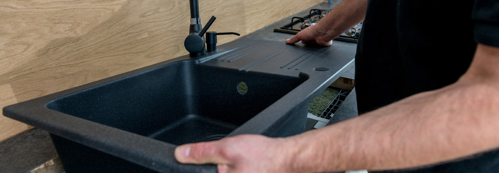 A person installing a new black sink in a kitchen.