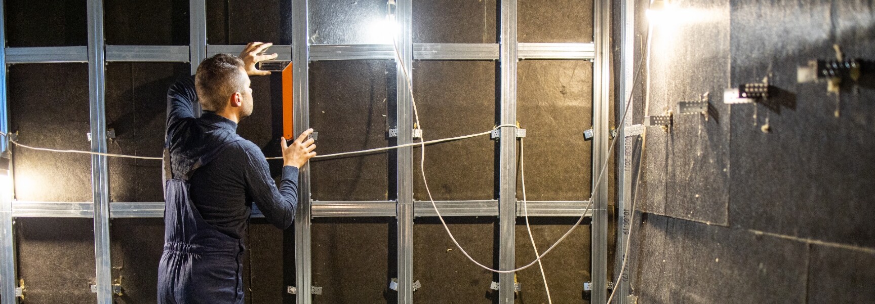 A person installing soundproofing material on a wall to reduce noise, using a roller to apply adhesive.