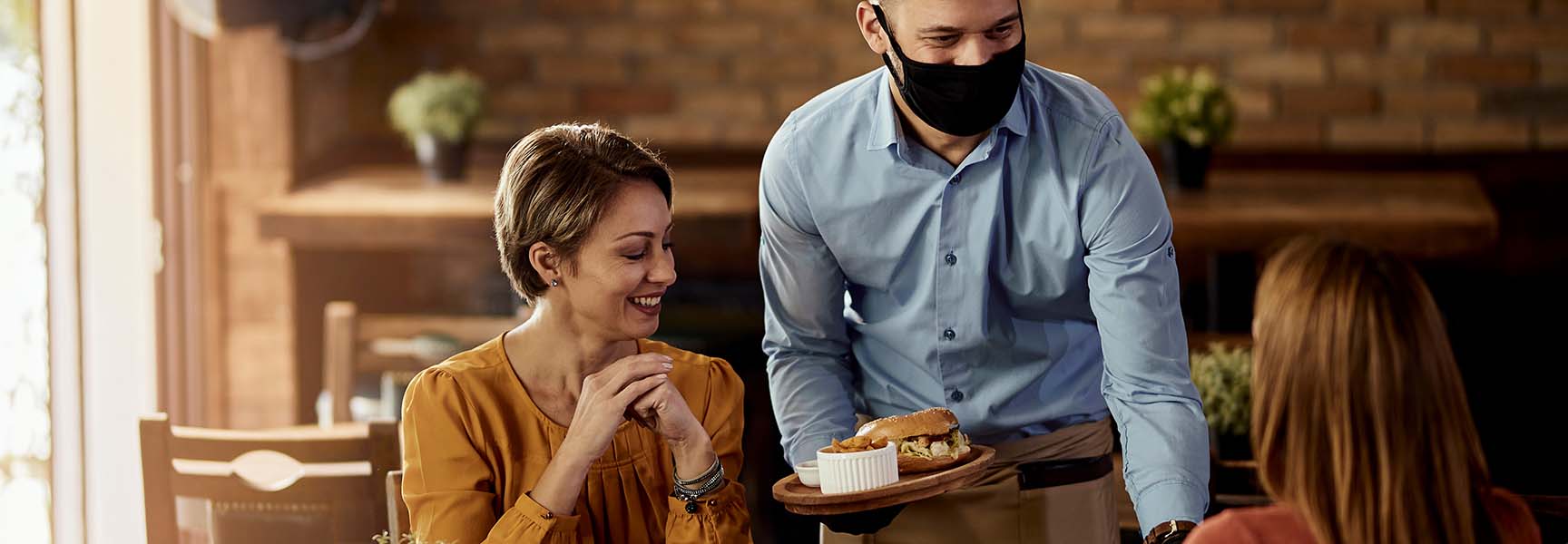 A waiter serving a sandwich and sides to 2 ladies in a cafe.