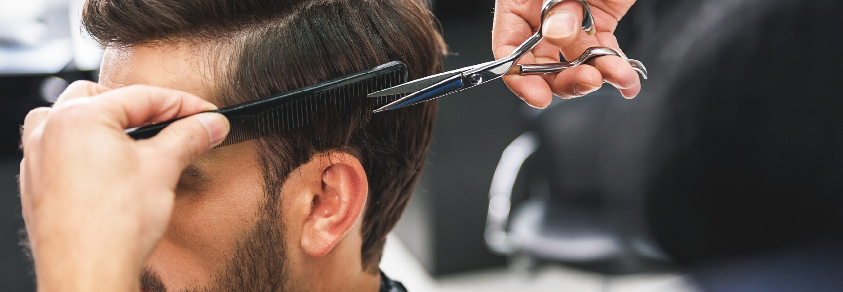 A mobile barber cutting a client's hair, trimming the side with a scissors and a comb.